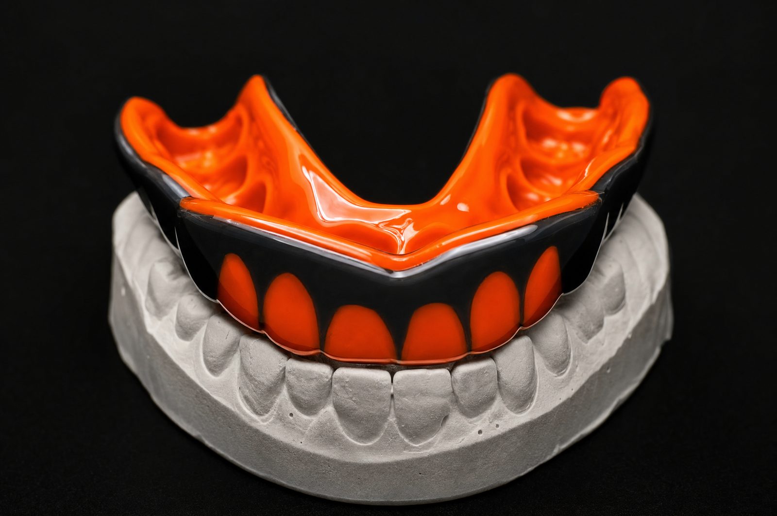 A custom orange and black FitGuard mouthguard on a dental model